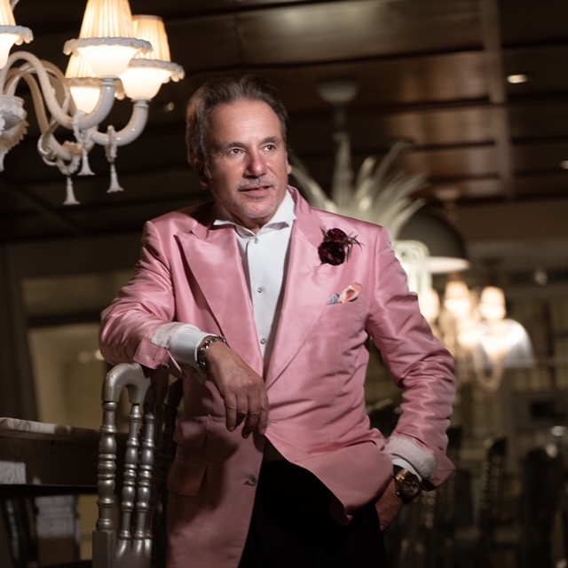 Joe Colangelo in a pink jacket beneath chandeliers, film noir lighting